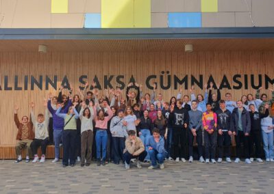Schülerinnen und Schüler vor einer Wand, auf der der Name des Gymnasiums in Tallinn steht.