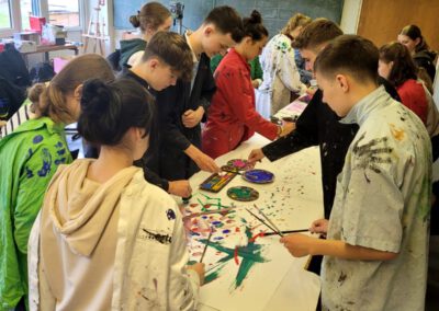 Schülerinnen und Schüler stehen gemeinsam am Tisch und malen ein Bild.
