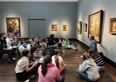 Kindersitzen in einem Kunstmuseum auf dem Boden und hören den Kuratoren zu.