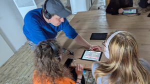 Kindersitzen in einem Kunstmuseum auf dem Boden und hören den Kuratoren zu.